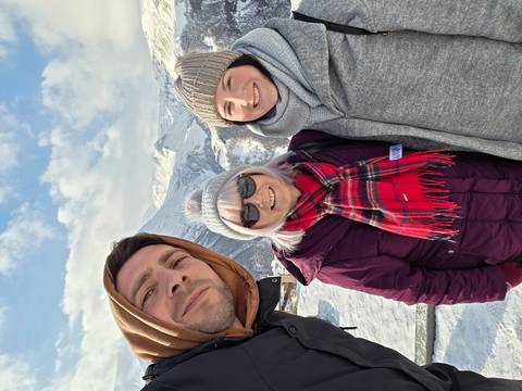       Three people posing with snow-covered mountains behind.
  
