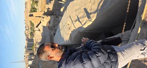       A man standing near ancient ruins with desert landscape in the background.
  