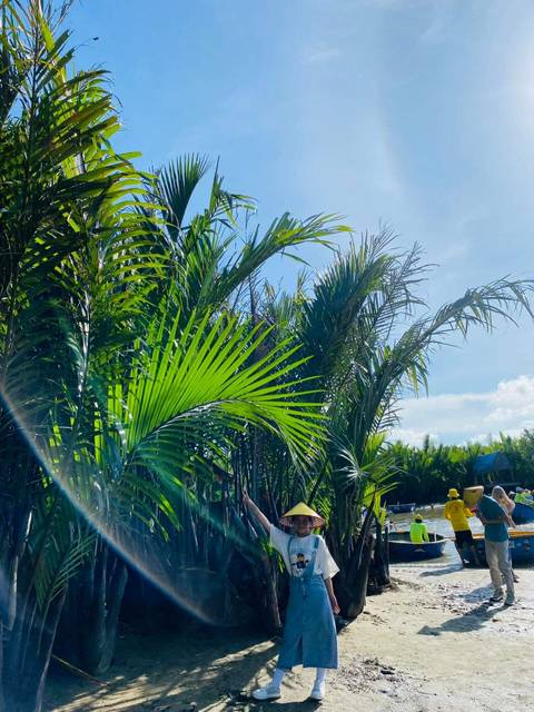 Lush green palm trees with people in the background under a clear blue sky.