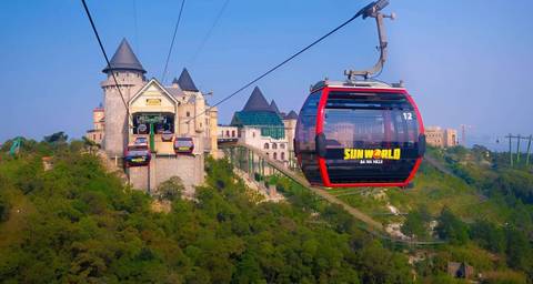       Cable cars moving towards a castle-like structure over forested hills.
  