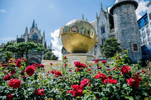       Golden globe structure with flowers in the foreground, surrounded by elaborate buildings.
  