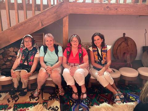 Four women sitting indoors with patterned shawls.