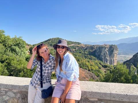 Two women posing with picturesque landscape of Meteora monasteries.