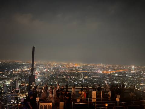       City skyline at night with illuminated buildings and people at a rooftop.
  