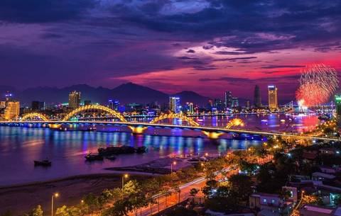Night view of a vibrant city with a bridge and fireworks.