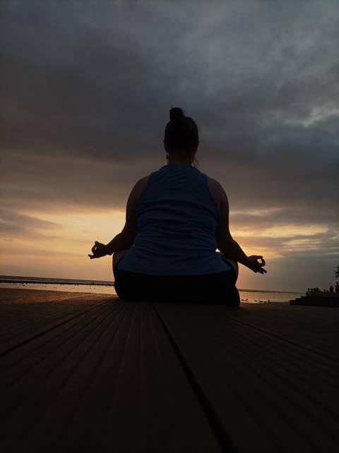 Silhouette of a person meditating during sunset by the sea.