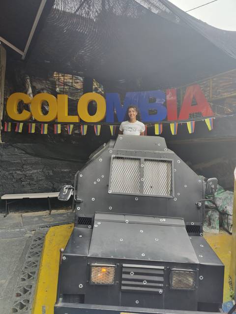 Person posing with a sign displaying 'Colombia' and a shielded vehicle.