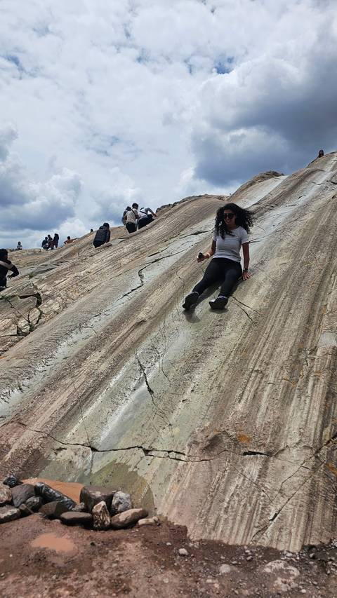 Person sliding down a rock formation with others nearby.