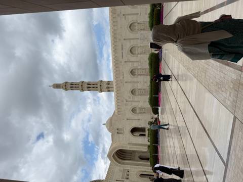 Exterior view of a mosque with a tall minaret and people walking.