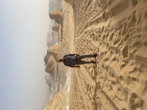 Person standing in a sandy desert landscape with rocky formations.