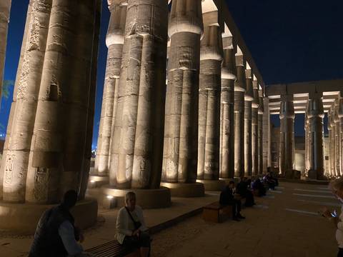 Well-lit columns of an ancient temple at night with people seated.