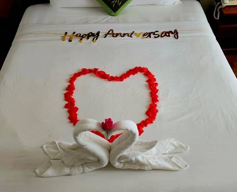 Bed decorated with a heart made of rose petals and towel swans for an anniversary celebration.