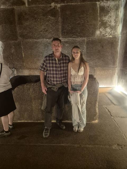       Two people posing inside a building with ancient stone structures.
  