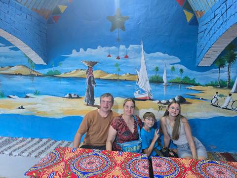       Family seated in a colorful room with mural paintings.
  