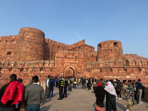       People outside Agra Fort, a large red sandstone fort
  