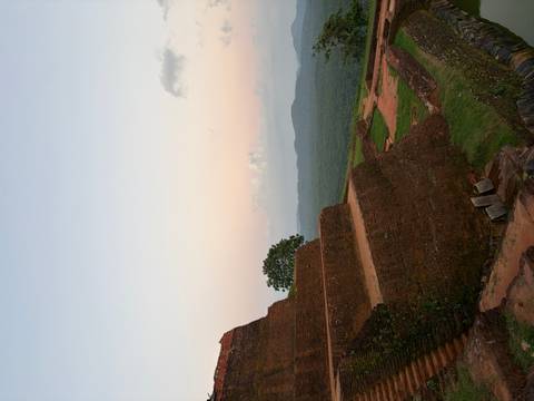 Sunset view from a high vantage point with ancient stone structures and distant greenery.