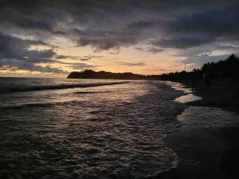 Beachfront at sunset with waves and silhouetted people.