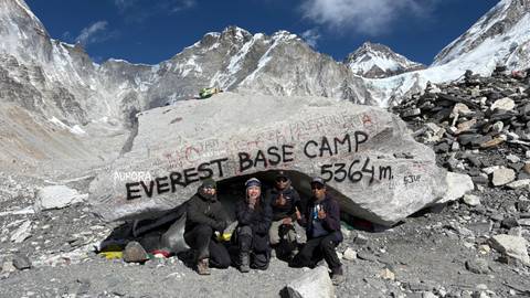 Group of people posing in front of a sign at a mountain base camp.