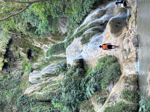       Person climbing a waterfall in a lush forest environment.
  