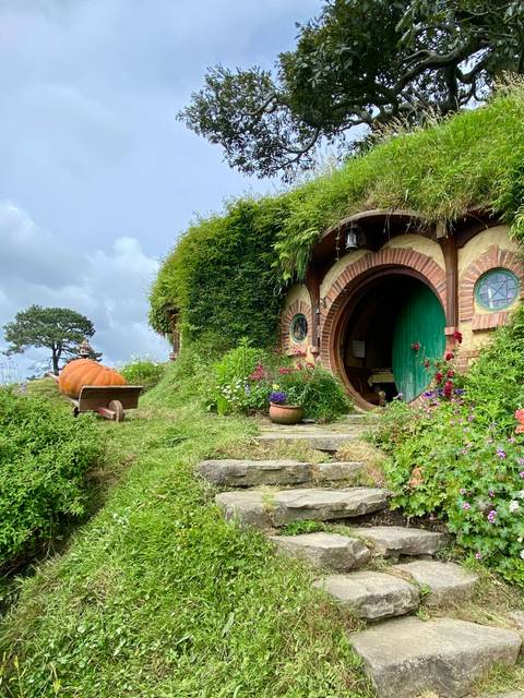 Quaint hobbit door surrounded by greenery and colorful flowers.