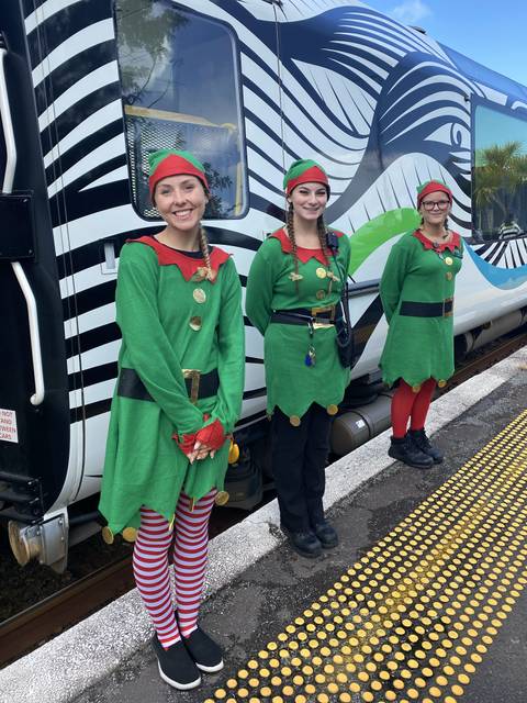       Three people dressed as elves standing next to a train.
  