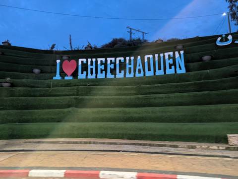       Landscape with a sign on a grassy terrace reading 'I love Chechaouen'.
  