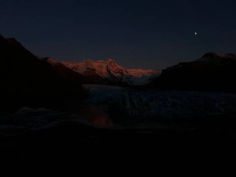 Dark landscape with a snowy mountain range at dusk.