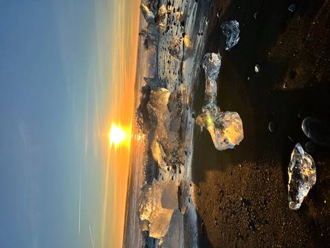 Glittering ice on a black sand beach at sunrise.