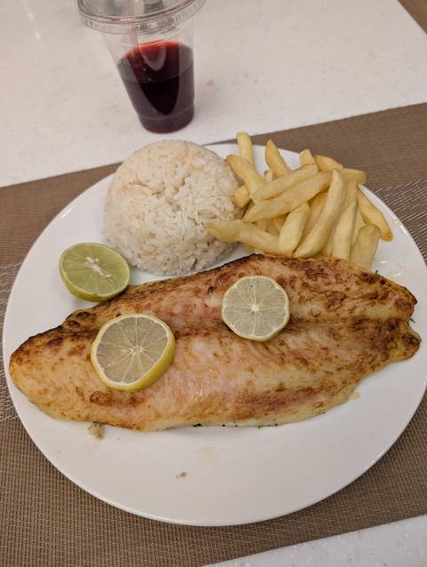 Plate of grilled fish with rice and fries, garnished with lemon.