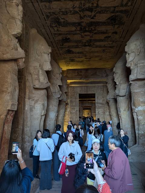 Interior of an ancient Egyptian temple with statues and people.