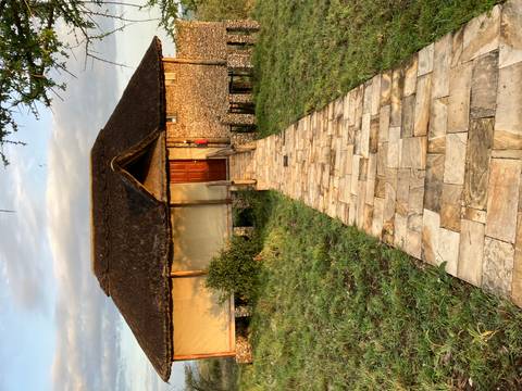       A thatched stone building with a paved pathway surrounded by greenery.
  