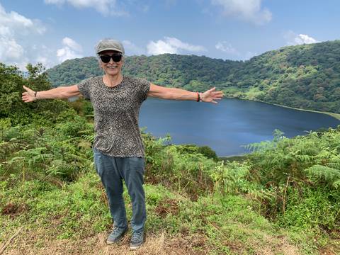 Woman posing with arms outstretched in front of a crater lake.