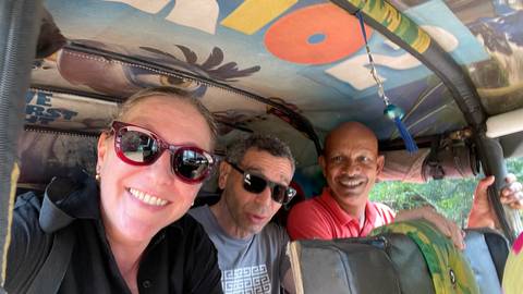       Three people smiling inside a tuk-tuk, viewed from inside.
  