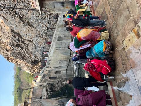       Group of people in colorful attire gathered by a water body.
  