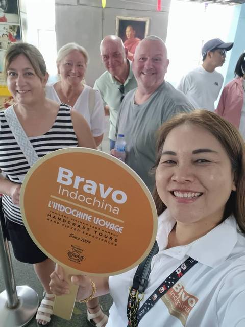       Group of tourists smiling with a tour guide and a sign for Bravo Indochina.
  