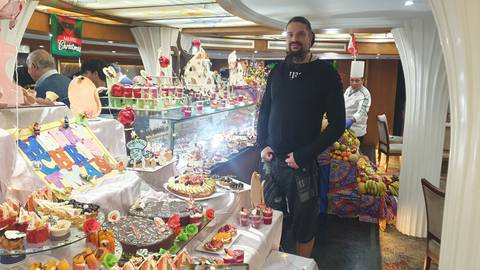 Indoor scene with a person smiling at a dessert buffet with a chef nearby.
