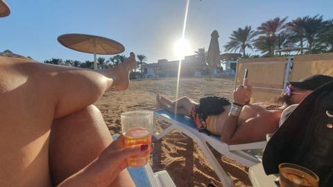 People relaxing on a beach with drinks in hand at sunset.