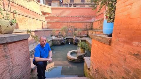       A person sitting near an ancient water fountain.
  