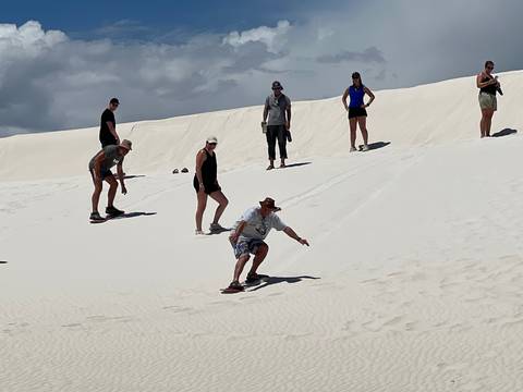       People sandboarding on a white sand dune.
  