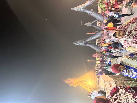 Visitors at night by large sculptures of praying hands.