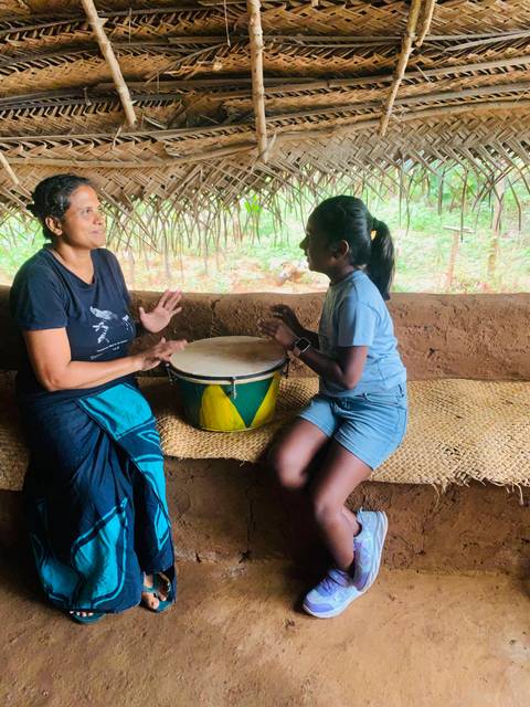 People playing a drum sitting on a mat.