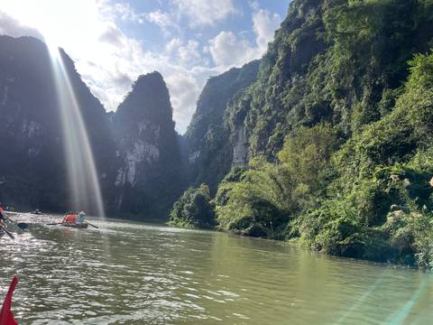 Sunlit river with lush limestone cliffs and a wooden boat.