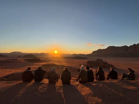       People sitting on a ridge watching the sunset over a desert landscape.
  