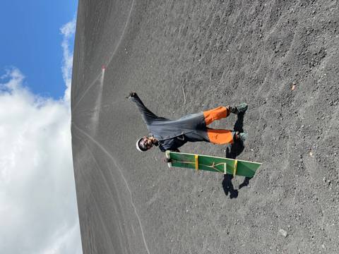       Person sandboarding down a volcanic slope.
  