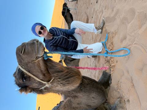 Person posing with a camel in the desert.