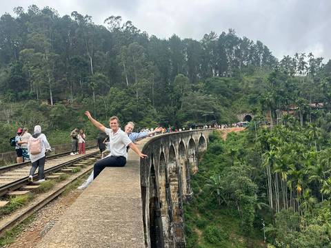 People posing on a railway bridge in a forested area.