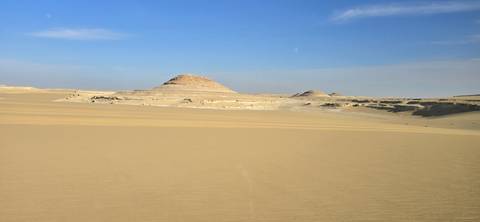 Desert landscape with small hills under a blue sky.