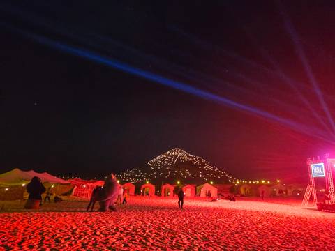       Night view with tents and people illuminated by red lights, with a lit mountain in the background.
  