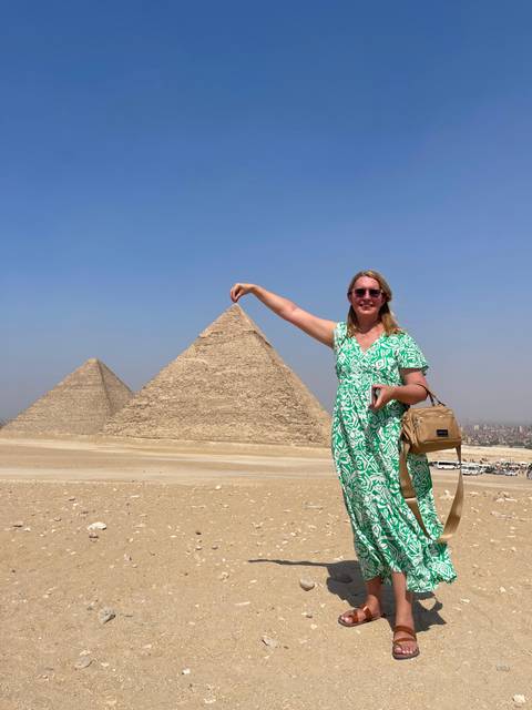       Woman posing as if holding the tip of a pyramid in front of the Giza Pyramids.
  