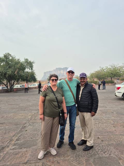       Three people posing outdoors with a fort in the background.
  